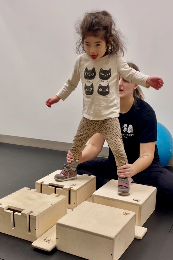Physiotherapist holding and balancing young child on her ankles walking on wooden boxes exercising Dynamic Movement Intervention