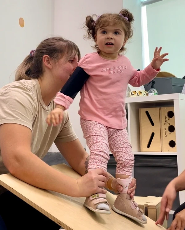 Physiotherapist holding and balancing young child with his feet on a slopped board exercising Dynamic Movement Intervention