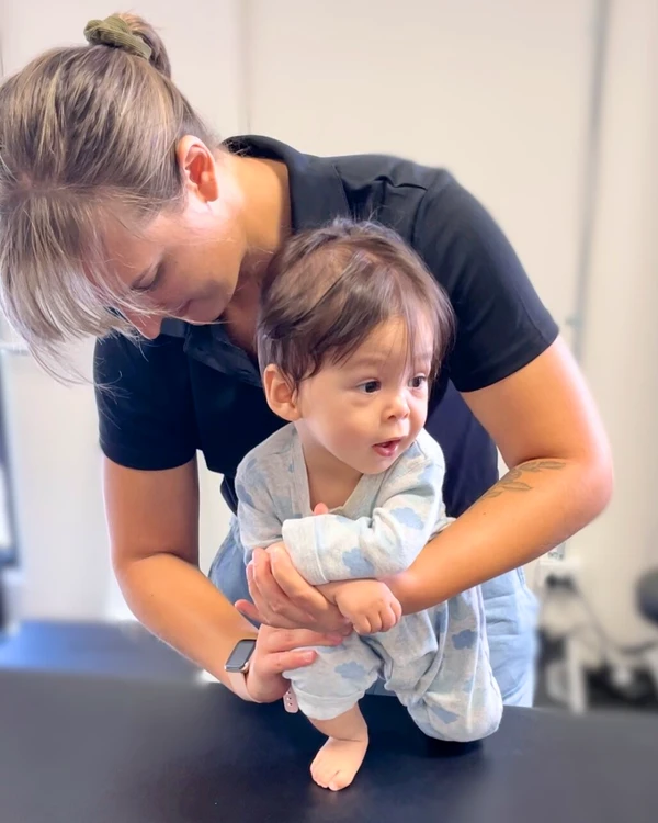 Physiotherapist holding and balancing young child pressing his lower leg down on a table