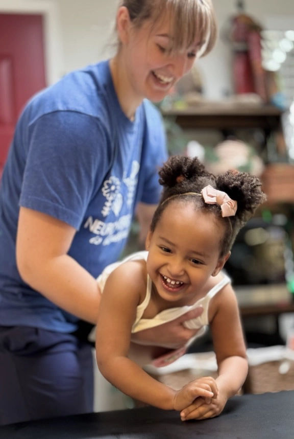 Physiotherapist holding and balancing young child with her belly on one hand stabilizing the upper body with the other hand, exercising Dynamic Movement Intervention