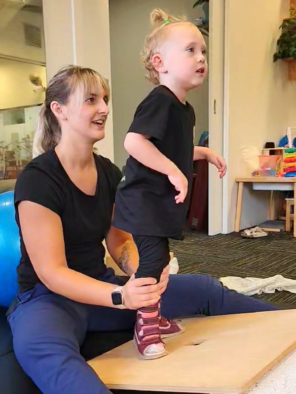 Physiotherapist holding and balancing young child with his feet on a slopped board exercising Dynamic Movement Intervention