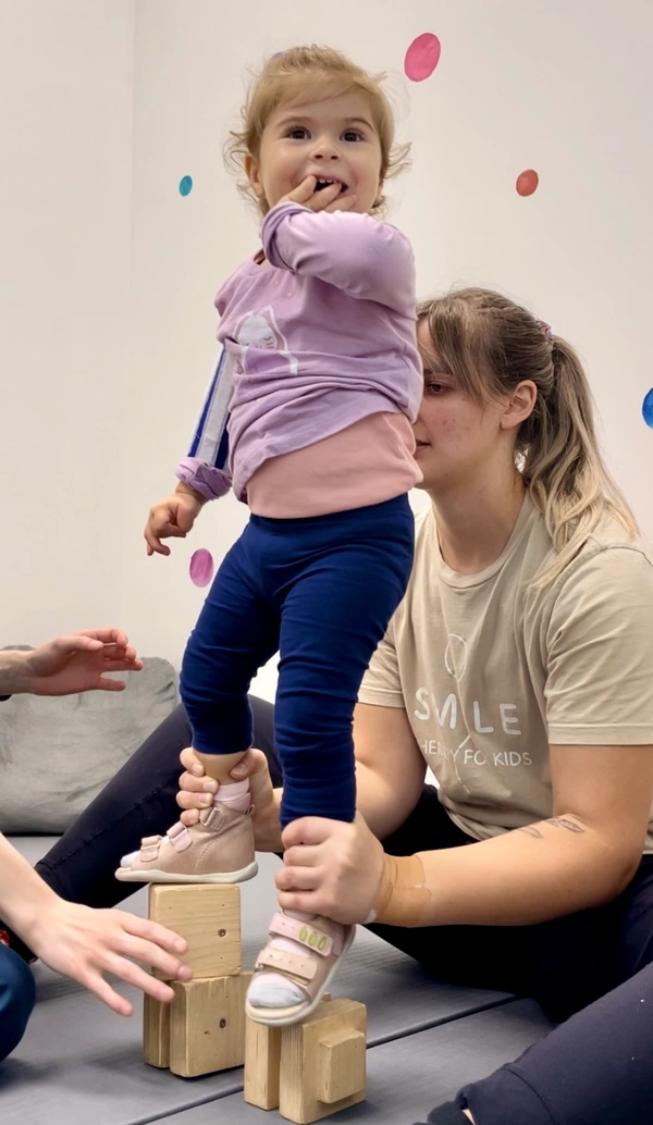 Physiotherapist holding and balancing young child with his feet on wooden blocks exercising Dynamic Movement Intervention