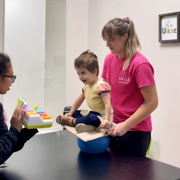 Physiotherapist holding and balancing young child sitting on a wooden board exercising Dynamic Movement Intervention