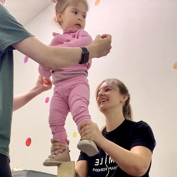 Physiotherapist holding and balancing young child with his feet on a wooden block exercising Dynamic Movement Intervention