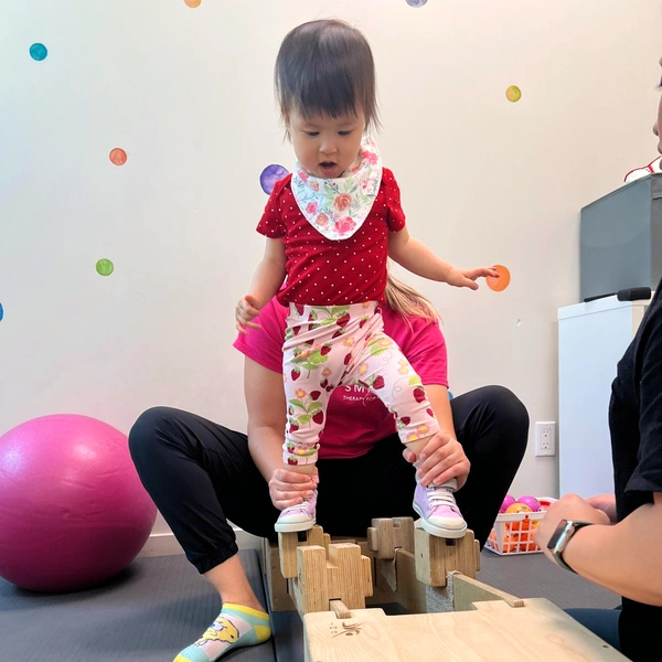 Physiotherapist holding and balancing young child with his feet on several wooden blocks exercising Dynamic Movement Intervention
