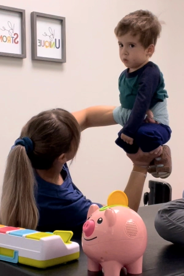 Physiotherapist holding and balancing young child with his lower legs on one hand stabilizing the upper body with the other hand, exercising Dynamic Movement Intervention